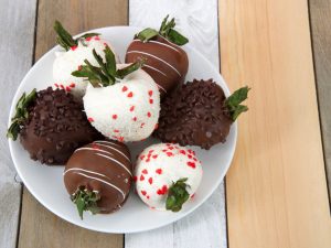Variety of Chocolate covered strawberries on a plate. Dark, white and milk chocolate on a wood table